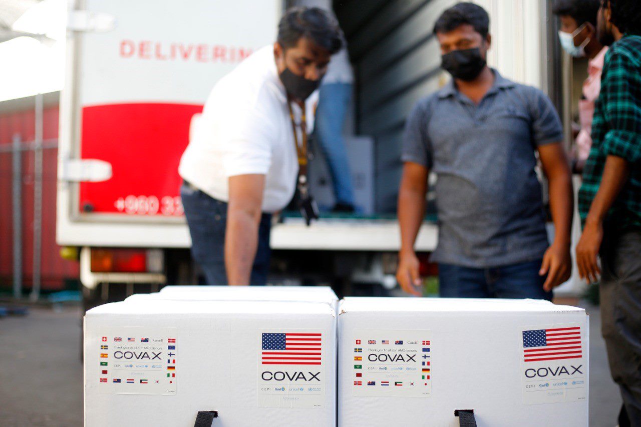 Two masked men stand over boxes of vaccines. 