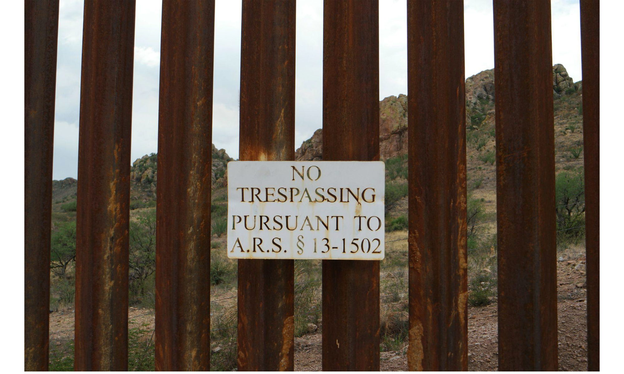 A sign on the border wall reads "No Trespassing Pursuant to A.R.S. 13-1502"