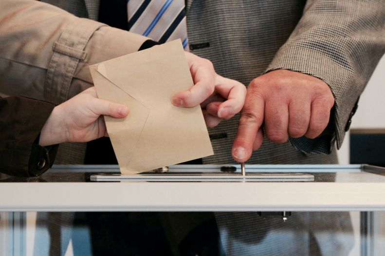 Hands placing a voting ballot into a receptacle.