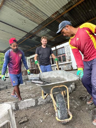 Dylan Rodgers pushes a wheelbarrow alongside two workers in Nepal. 