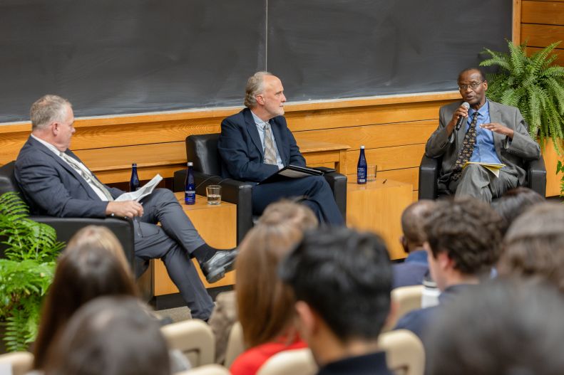 Chris Barrett speaks into a microphone next to Paul Kaiser and Chris Barrett.