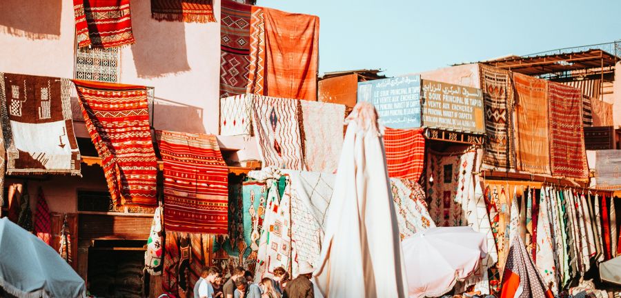 Bright orange and red rugs hang over buildings in Marrakesh.