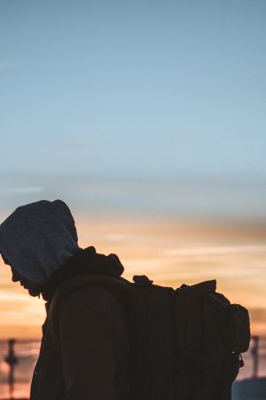 silhouette of person carrying backpack at orange sunset