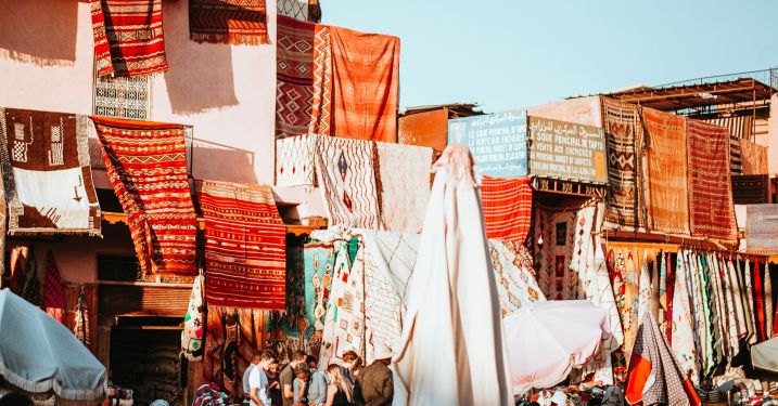 Bright orange and red rugs hang over buildings in Marrakesh.