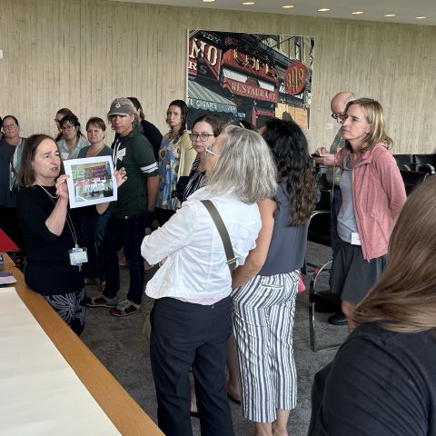 A museum staff person shows a work of art to a group of standing teachers.