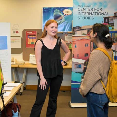 Global Scholar Mira DeGregory stands and talks with a student in front of her painting at the student showcase.