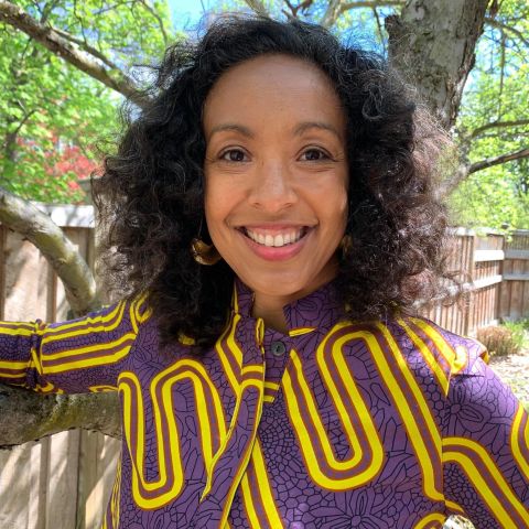 Christa Nuñez smiles, holding her arms out to hold the phone camera for a selfie. 