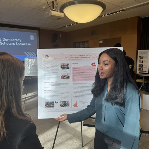 Global scholar gestures toward a research poster while speaking to someone about the project.