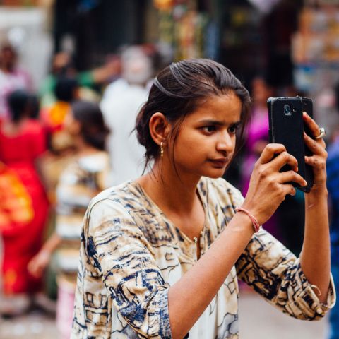 Indian woman holds up phone to take pictures.