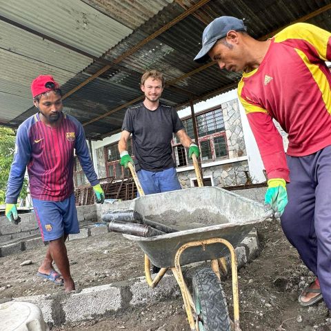 Dylan Rodgers pushes a wheelbarrow alongside two workers in Nepal. 