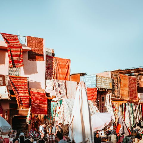 Bright orange and red rugs hang over buildings in Marrakesh.